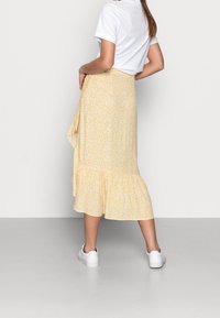Gonna midi gialla a fiori con orlo volants, realizzata in tessuto leggero. Indossata con una t-shirt bianca e abbinata a sneakers bianche.