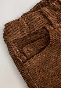 Tessuto di corduroy marrone con una trama a coste verticali, caratterizzato da una vita e dettagli delle tasche laterali. Accenti cuciti lungo le cuciture.