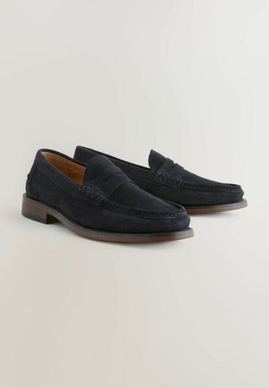 Marineblå ruskinds loafers med et tekstureret læderbånd, lavt træhæle og dekorative syninger, der viser et klassisk slip-on design.