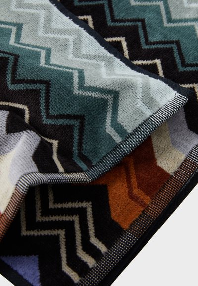 Covor cu un model zigzag multicolor, featuring nuanțe de teal, negru, portocaliu și bej. Material moale și texturat, cu o margine închisă la culoare și accente în dungi.
