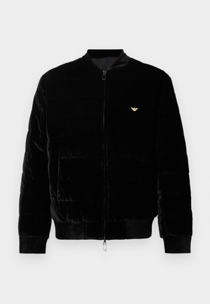 Czarna kurtka bomberka z zamkiem błyskawicznym, wykonana z pluszowego materiału. Posiada poziomy pikowany wzór, ściągacze na mankietach oraz małe złote logo na piersi.