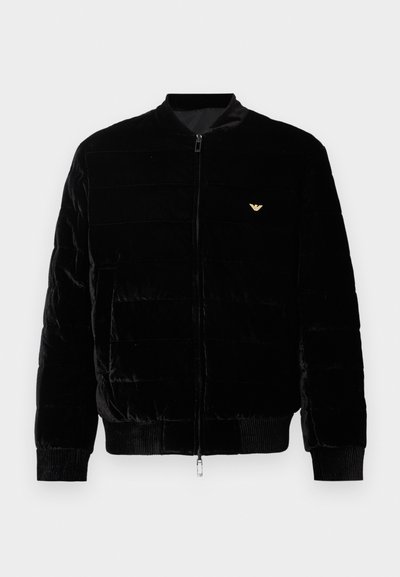 Μαύρο bomber μπουφάν με φερμουάρ, κατασκευασμένο από απαλό βελούδινο υλικό. Διαθέτει οριζόντιο καπιτονέ σχέδιο, ριμπ μανσέτες και μικρό χρυσό λογότυ�πο στο στήθος.