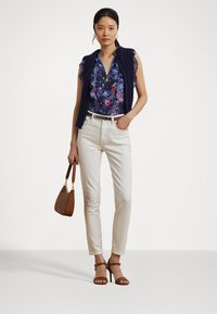 Floral-patterned blouse in blue, white sleeveless top under a navy knit vest, white fitted pants, brown handbag, and brown heeled sandals.