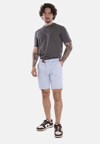 Outfit maschile composto da una maglietta grigia a maniche corte e pantaloni corti azzurri chiari con cintura. Scarpe sportive con una combinazione di colori marrone e beige.