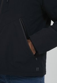 Musternakk, millel on tõmblukuga tasku ja sile, matt viimistlus. Reguleeritavad varrukad ja minimalistlik logo detail helmel.