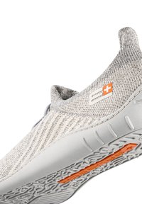 Lekki, szary, dzianinowy but sportowy z teksturowaną cholewką, gumową podeszwą i pomarańczowym akcentem na podeszwie. Posiada projekt slip-on.