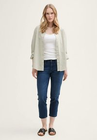 Világoszöld és fehér csíkos, gombos ing, fehér trikó fölött viselve, sötétkék, rövidített farmernadrággal és fekete szandállal párosítva.