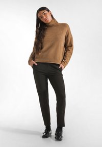 Suéter de cuello alto de lana marrón combinado con pantalones negros a rayas; ambos presentan cortes relajados y acabados texturizados. Mocasines negros completan el look.