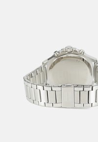 Silberne Edelstahl-Uhr mit einem Gliederarmband, runder Gehäuseform und einem polierten Boden. Verfügt über eine Krone und Chronographenknöpfe.
