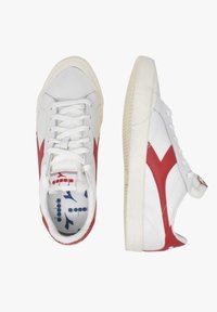 Sneakers bianchi con accenti rossi, suole in gomma testurizzata e design con lacci. Presentano un logo sulla linguetta e un motivo distintivo sui lati.