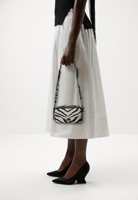 Bolso de mano con estampado de cebra en blanco y negro, con una textura suave, cierre de cremallera y una correa delgada. Situado frente a un fondo blanco.