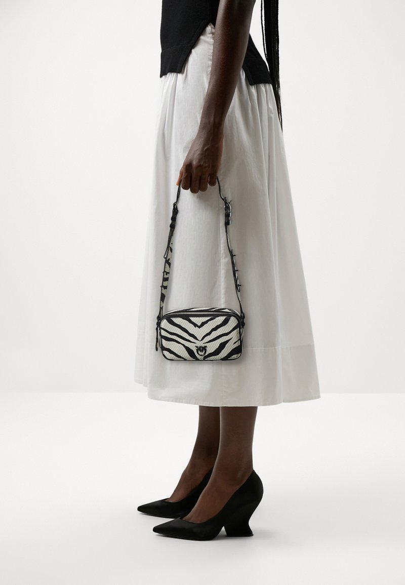 Bolso de mano con estampado de cebra en blanco y negro, con una textura suave, cierre de cremallera y una correa delgada. Situado frente a un fondo blanco.
