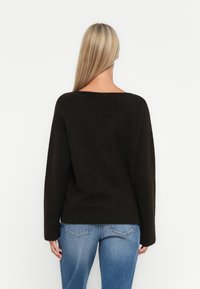 Svart, oversized genser med vid halslinning og ribbestrikket kant, kombinert med lyseblå jeans, som viser et mykt og teksturert stoff.