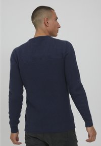 Mornarsko moder pleten jumper z teksturiranim vzorcem na zgornjem delu hrbta in gladkimi rebrastimi manšeti ter robom, z dolgimi rokavi in okroglim izrezom.