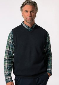 Námořnická vesta vyrobená z pletené tkaniny, vrstvená přes košili s dlouhým rukávem v zeleno-modré kostce. V-krční design s žebrovaným lemem.