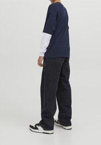 Marinblå t-shirt med kort ärm över en vit långärmad skjorta, som är kombinerad med svarta jeans och svartvita sneakers.