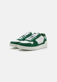 Zöld velúr sneaker fehér bőr részletekkel, kerek orr, fehér fűzőkkel. Texturált oldalakkal és párnázott talppal rendelkezik. Kiemelkedő logó részlet.