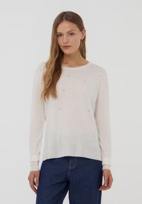 Maglione bianco a maniche lunghe con tessuto testurizzato, caratterizzato da piccole decorazioni sulla parte anteriore e una vestibilità rilassata. Maniche con polsini, orlo arrotondato.