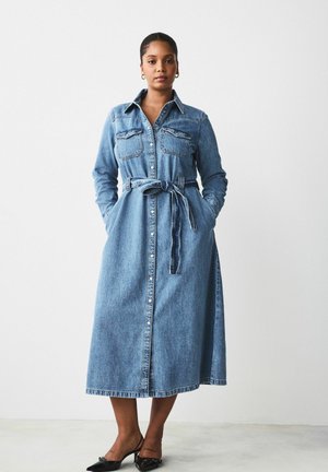 Robe en denim à manches longues, avec un devant boutonné, deux poches poitrine, une taille ceinturée et une longueur maxi. Couleur bleu clair et texture douce.