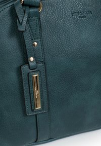 Borsa a tracolla verde in pelle con superficie testurizzata, hardware color oro e una targhetta decorativa. Chiusura con zip e tracolla regolabile mostrata.