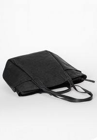 Black leather tote bag with dual handles, slightly folded, resting on a white surface with visible zipper detail.