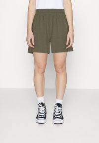 Shorts côtelés vert olive avec une taille élastique, coupe droite et poches latérales, associés à des baskets montantes noires et des chaussettes blanches.