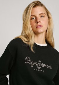 Sudadera negra en mezcla de algodón, con un logo bordado en blanco "Pepe Jeans LONDON" en el pecho. Cuello redondo y puños acanalados.