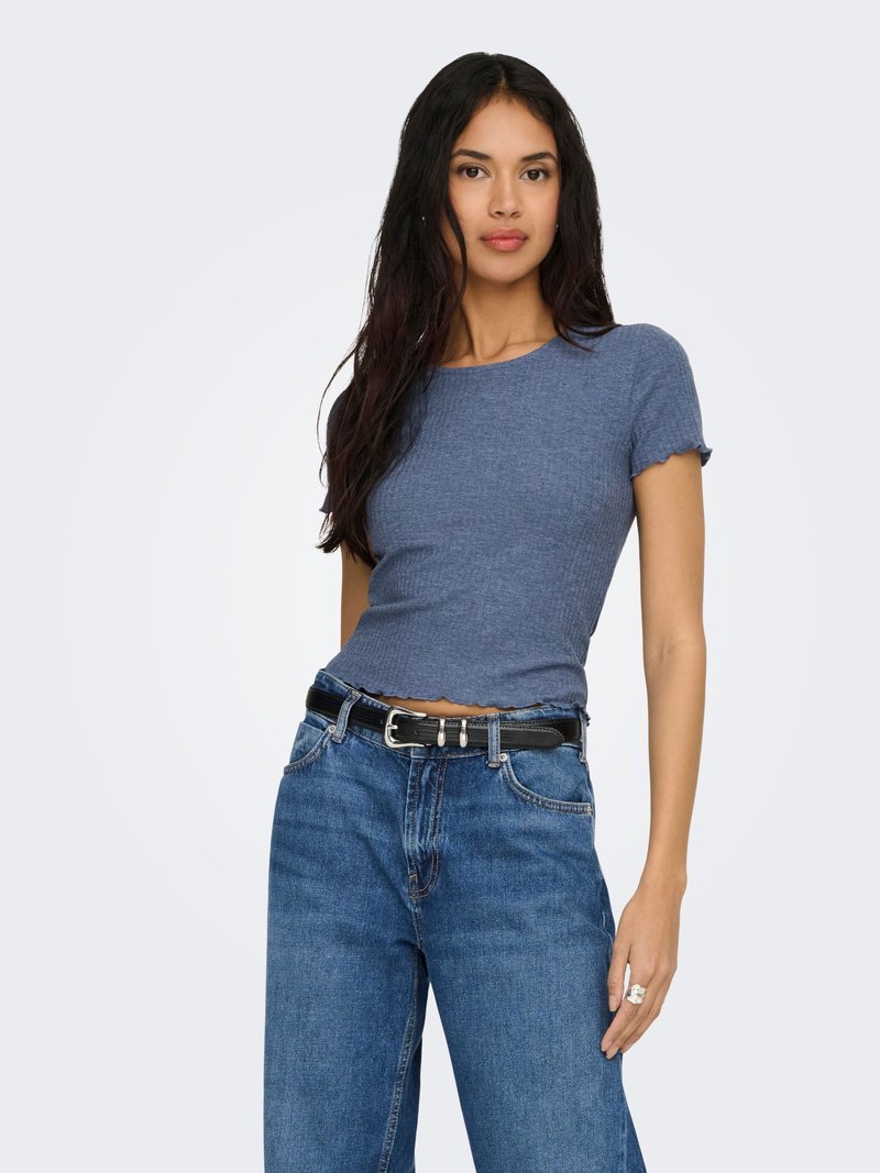 Femme aux longs cheveux noirs portant un haut bleu ajusté à manches courtes avec un ourlet ondulé et un jean bleu taille haute avec une ceinture noire.