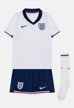 Jersey blanca de manga corta con acentos en azul marino, que presenta el emblema de Inglaterra y un logo de Nike. Incluye pantalones cortos azul marino y calcetines blancos con rayas rojas.