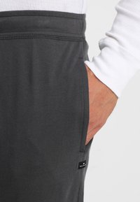 Grijze katoenen joggers met een zijzak en een zichtbaar etiket. De stof heeft een gladde textuur met gestikte details bij de tailleband.