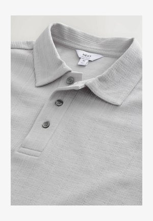 Svetlo siva polo majica iz teksturiranega materiala, z ovratnikom, tremi gumbi in preprosto zasnovo z diskretnimi vzorci.
