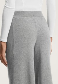 Sive pletene hlače z širokimi nogavicami, ki imajo rebrast pas in stranske šive. Tekstura je mehka in gladka, primerna za sproščeno nošenje.