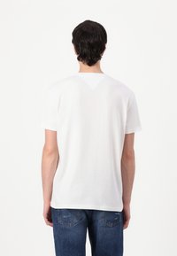 White t-shirt with a classic crew neck, short sleeves, and a subtle triangular stitch detail at the back. Paired with blue denim jeans.