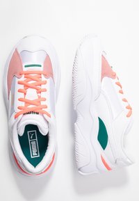 Weiße Sportschuhe mit rosa Akzenten. Merkmale sind eine strukturierte Sohle, Schnürsenkel in leuchtendem Orange und ein grünes Logo-Detail auf der Lasche.