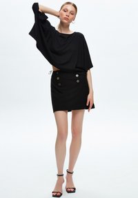Top negro de corte holgado con mangas cortas y longitud recortada, combinado con una falda negra con botones decorativos y un diseño elegante.