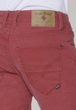 Rdeče jeans hlače z teksturiranim zaključkom, izraziti zadnji žepi s detajli šivanja ter usnjena oznaka blagovne znamke na pasu.