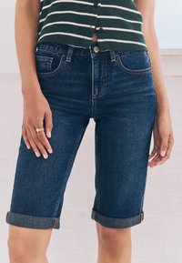 Pantaloni scurți Bermuda din denim albastru închis, cu un design conic, tivuri întoarse, detalii cusute și buzunare frontale.