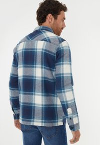 Rutig flannel skjorte i blå, hvid og grå nuancer. Har knaplukning fortil, lange ærmer og krave. Blød tekstur med klassisk ternet mønster.