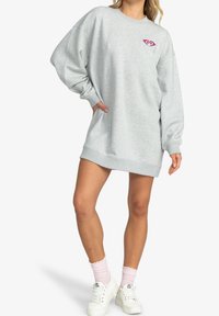 Vestido sudadera gris con corte holgado, puños acanalados y un logo de corazón rosa en el pecho. Textura suave y longitud corta.