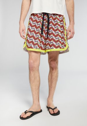 Pantaloni da bagno rossi e bianchi con motivo geometrico, dotati di un laccio di chiusura nero, rifiniture gialle e una vestibilità ampia.