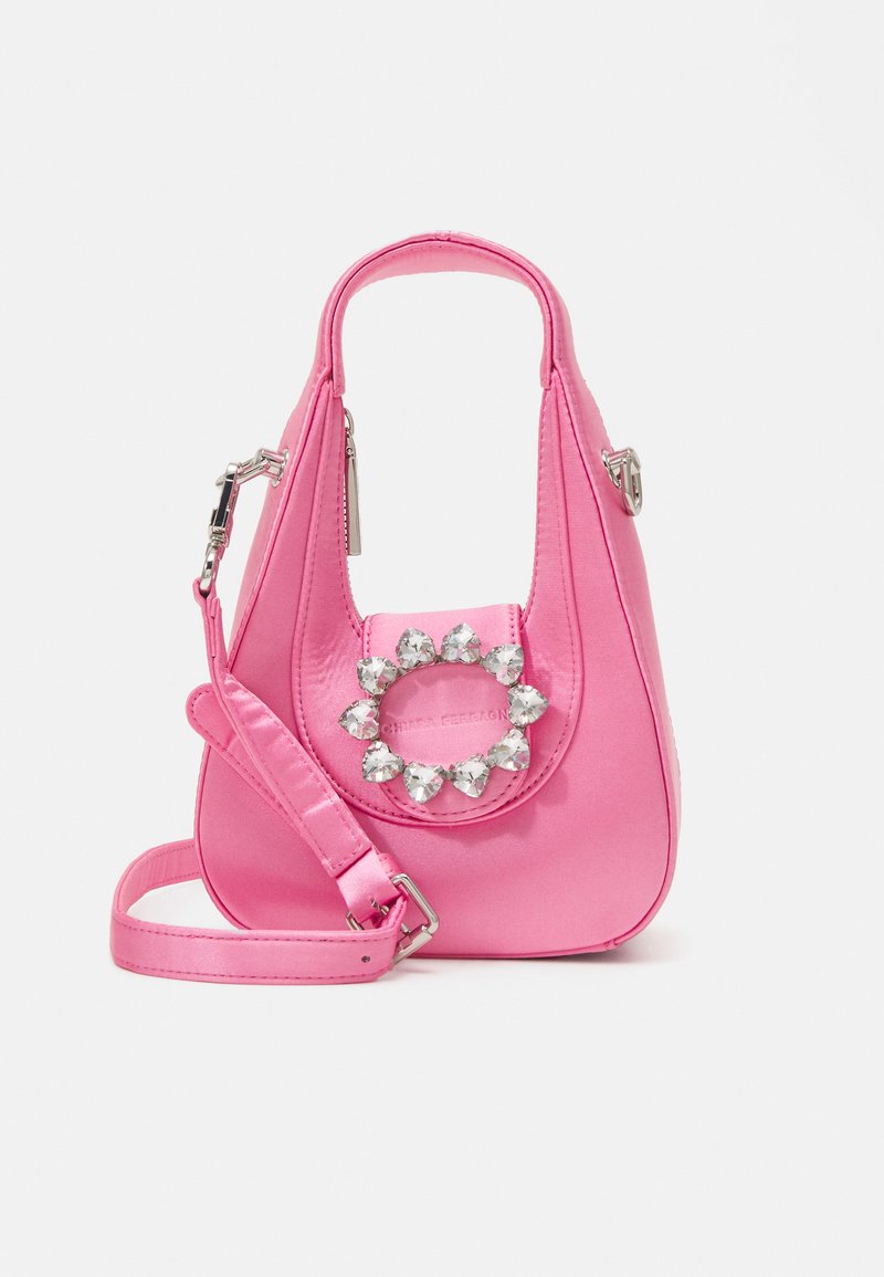 Sac en satin rose avec une forme courbée, mettant en avant un accent circulaire orné de pierres précieuses et une bandoulière amovible.