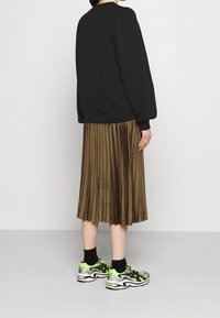 Svart tröja, plisserad brun midikjol och livfullt gröna och svarta sneakers. Outfiten kombinerar slät tyg och strukturerade designelement.
