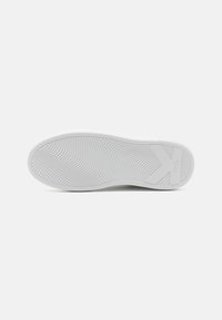 Fehér gumis sneaker talp textúrált hullámokkal és barázdákkal a tapadás érdekében, az oldalán kiemelkedő logóval és sima, lekerekített szélekkel.