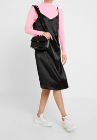 Vestito in satin nero con spalline sottili, sovrapposto a un dolcevita rosa aderente. Abbinato a sneakers bianche e a una piccola borsa a tracolla nera.