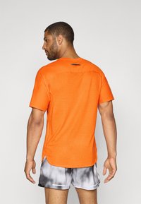 T-shirt atletico arancione con schiena traspirante perforata, colletto rotondo e orlo leggermente più lungo sul retro.