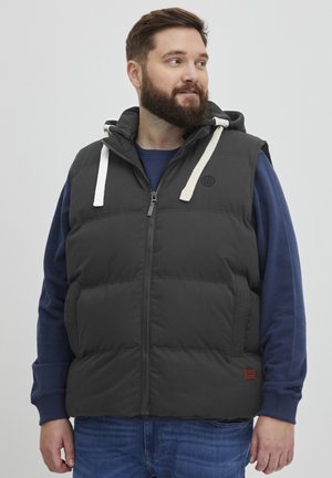 Black padded vest with a hood, featuring white drawstrings, zippered front, side pockets, and a textured fabric. Worn over a blue long-sleeve shirt.