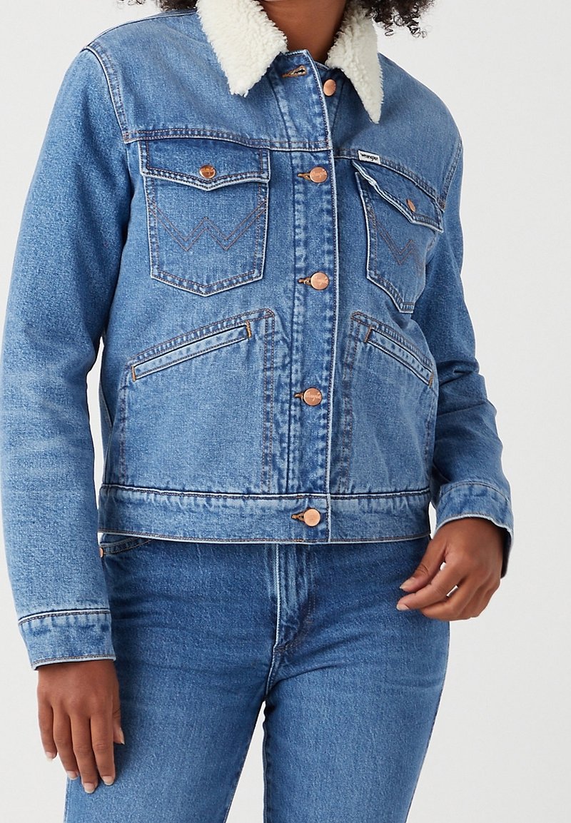 Jeansjacka med ljusblå tvätt, faux shearling-krage, kopparknappar, två bröstfickor och kontrasterande sömnadsdetalj.