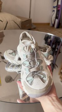 White athletic shoes with mesh panels and light blue accents. Features a rounded toe, textured sole, and elastic lacing system.