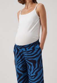 White sleeveless top with adjustable straps and blue pajama pants featuring a dark blue zebra stripe pattern and elastic waistband.