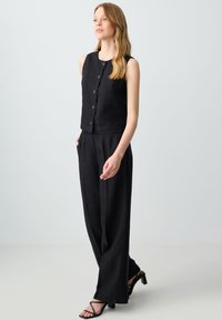 Completo in lino nero composto da top senza maniche con bottoni e pantaloni a gamba larga. Il design è minimalista con una finitura testurizzata.